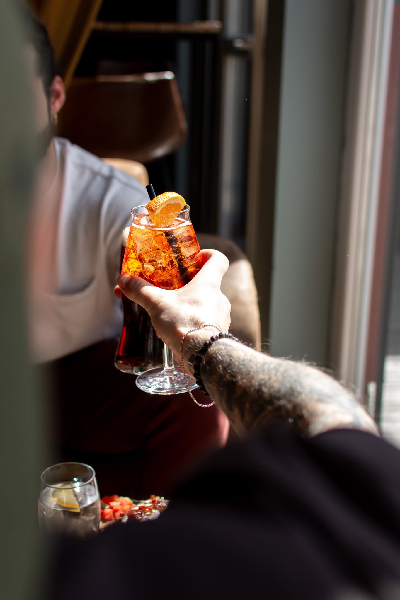 Gast hebt in der Vista Bar ein Glas mit Aperitif; dahinter der renovierte Innenraum mit Fensterfront.