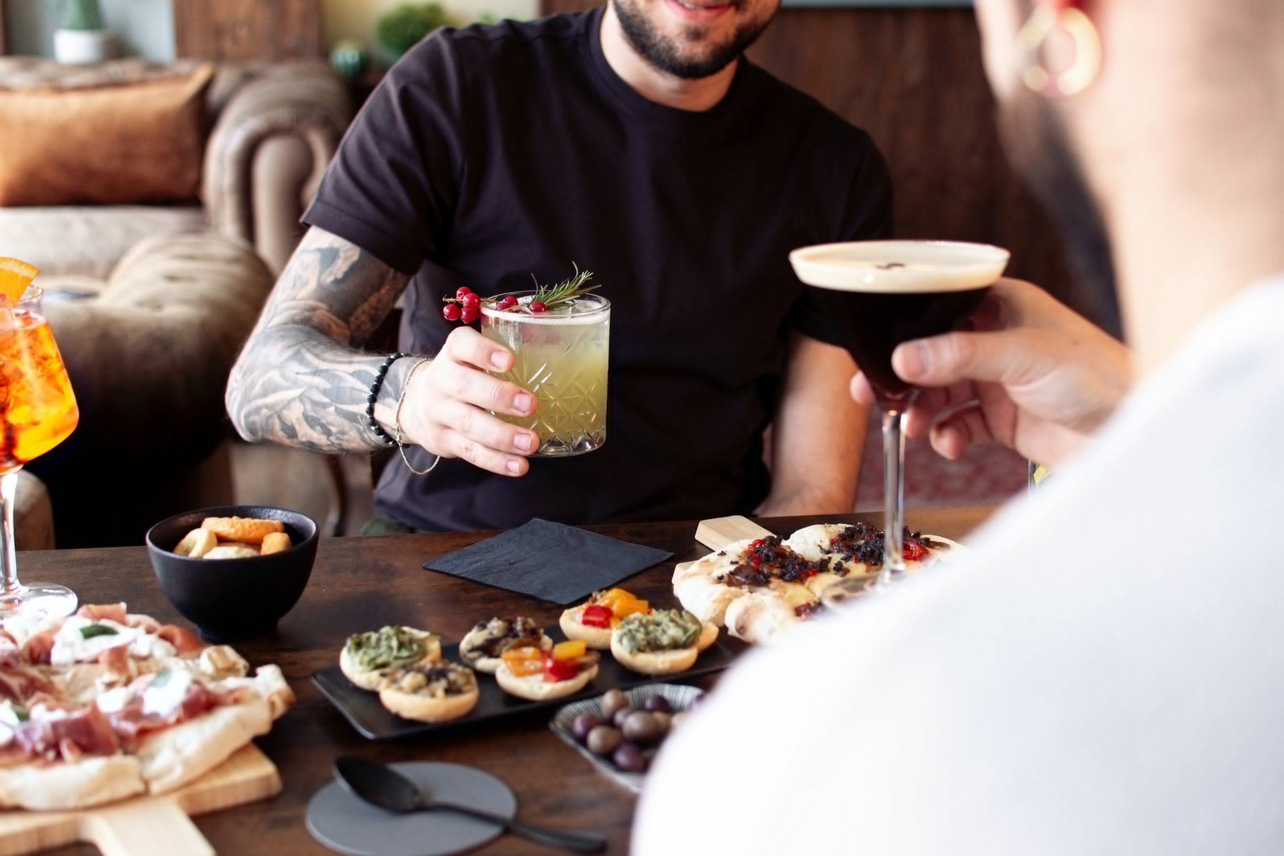 Zwei Gäste sitzen im Gespräch am Tisch der Vista Bar, mit Drinks und kleinen Speisen zwischen sich.